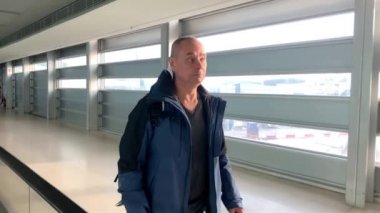 Sırt çantalı bir turist havaalanı lobisinin parlak binası boyunca gider, büyük pencerelerden sokağa bakar, uçuş ve seyahat için bekleme konsepti