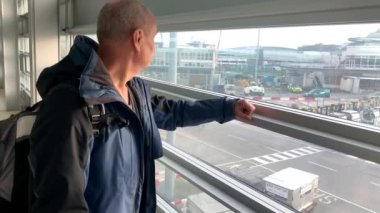 Parlak bir havaalanı binasında bir adam pencerenin önünde bekliyor ve sokağa bakıyor. Seyahat konsepti.