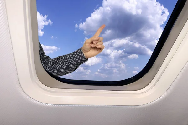 Mano masculina muestra en el fondo un hermoso paisaje celestial de cielo azul con nubes esponjosas detrás del ojo de buey de un avión, concepto de viaje —  Fotos de Stock