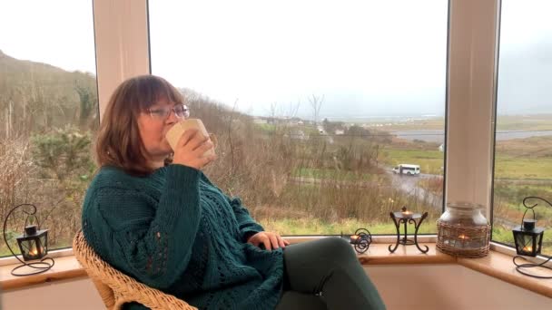 女人坐在阳台上舒适的柳条椅上 喝着热茶 朝窗外看去 这是一个享受和放松的概念 — 图库视频影像
