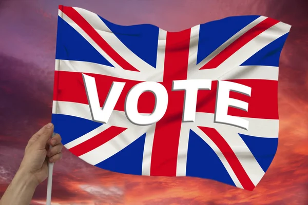 Hand holds against the background of the sky with clouds the colored flag of Great Britain on a luxurious texture of satin, silk with waves, closeup, copy space — Stock Photo, Image