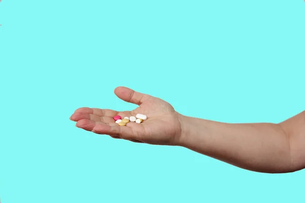 Female hand holds out, offering, a handful of colored pills and capsules, close-up, color background, copy space, concept of medical care, treatment — Stockfoto