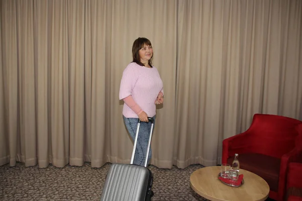 Горизонтальная фотография туристки, стоящей в гостиничном номере с чемоданом у окна, туристическая концепция — стоковое фото