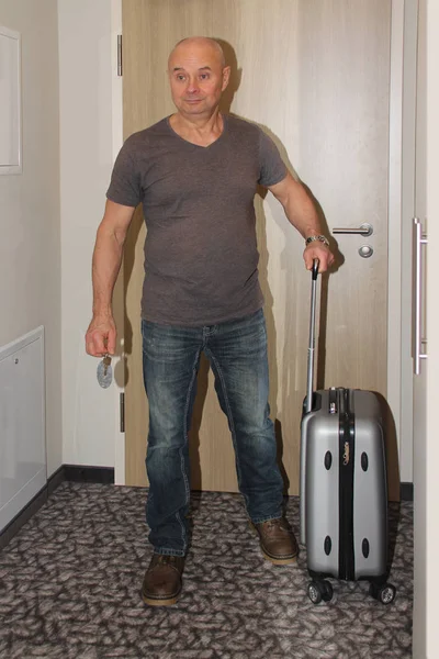 Ενήλικος άνδρας στέκεται σε ένα δωμάτιο ξενοδοχείου στην πόρτα με μια βαλίτσα και τα κλειδιά στο χέρι του, η έννοια της μια πολυαναμενόμενη διακοπές, επαγγελματικό ταξίδι — Φωτογραφία Αρχείου