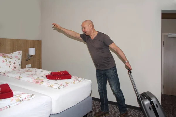 Un hombre con una maleta está de pie en una habitación de hotel y quiere saltar a la cama, concepto de vacaciones, viaje de negocios —  Fotos de Stock