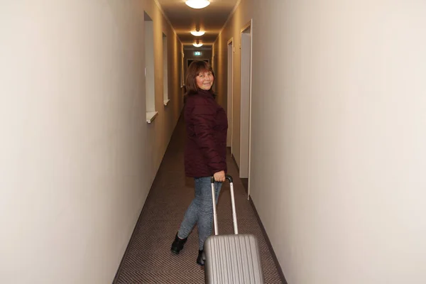 Foto horizontal de una mujer, un turista, caminando a lo largo de un largo pasillo del hotel con una maleta más allá de la puerta, concepto turístico —  Fotos de Stock