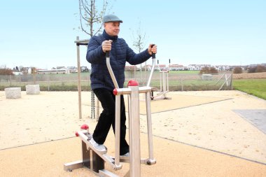 Orta yaşlı bir adam sokak egzersiz makineleri üzerinde fiziksel egzersiz yapıyor, farklı yaşlardaki spor konsepti, fiziksel aktivite, sağlıklı yaşam tarzı.