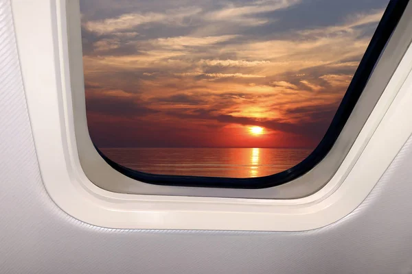 Beautiful sky landscape of red sunset with clouds and sea below through the porthole of a plane, travel concept — 스톡 사진