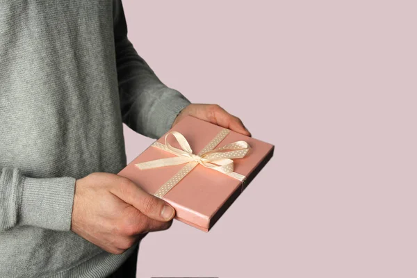 Mężczyzna trzyma prezent w ręku w różowym pudełku z satynową wstążką na jasnym tle, koncepcja wakacje — Zdjęcie stockowe