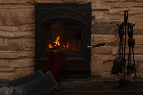 Pernas masculinas em jeans e meias vermelhas escuras perto do fogo quente de uma lareira em chamas, conceito de relaxamento no inverno e outono — Fotografia de Stock