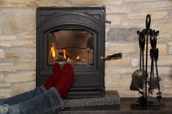 Pernas masculinas em jeans e meias vermelhas escuras perto do fogo quente de uma lareira em chamas, conceito de relaxamento no inverno e outono — Fotografia de Stock