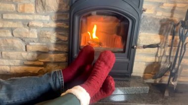 Erkek ve kadın yanan bir şöminenin yanında uzanır, bacakları kırmızı çoraplarla ateşe uzanır, kış rahatlama kavramı.