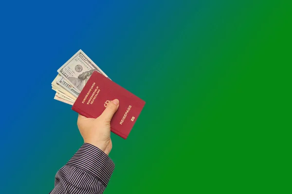 A man’s hand holds a Germany passport with dollars in dollars on a blue, green background — Stock Photo, Image