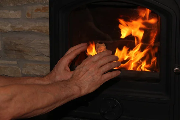 Homem de meia-idade sentado perto de uma lareira quente, braços estendidos para o fogo, conceito de humor de inverno — Fotografia de Stock