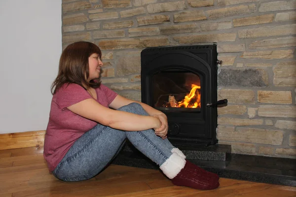 Mulher sentada perto de uma lareira ardente e olhando para o fogo, conceito de humor de inverno — Fotografia de Stock