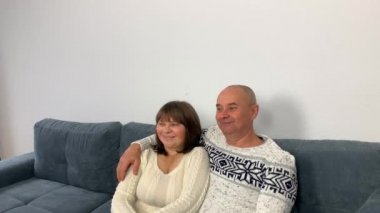 İskandinav beyaz kazaklı yetişkin bir adam ve kanepede oturan ve televizyon izleyen bir kadın.