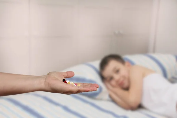 Mano femenina extiende, ofreciendo, un puñado de píldoras y cápsulas de color, primer plano, imagen borrosa de un niño acostado en el fondo, espacio de copia, concepto de atención médica, tratamiento —  Fotos de Stock