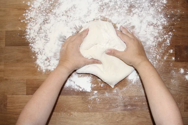 Female hands knead the dough on a wooden table, sprinkled with flour, close-up, selective focus, home cooking concept, copy space — Stock Photo, Image