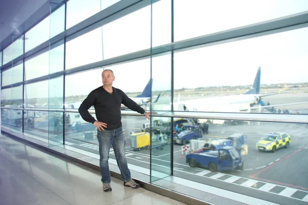 Homem, um passageiro, esperando por seu voo, fica na janela e olha para a pista do aeroporto, um concerto de viagem — Fotografia de Stock