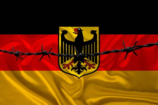 Järn taggtråd mot bakgrund av den nationella silkesflaggan i Tyskland med vapensköld, begreppet fängelse för lagbrytare, för belägringsområdet — Stockfoto