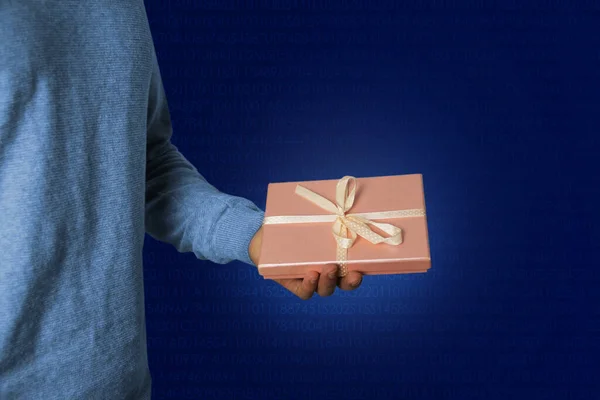 Mężczyzna trzyma prezent w ręce w różowym pudełku z satynową wstążką na niebieskim tle technologii, koncepcja wakacje — Zdjęcie stockowe
