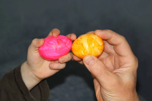 Ребенок держит одно розовое яйцо в руке, взрослый имеет желтый, концепция пасхального веселья — стоковое фото