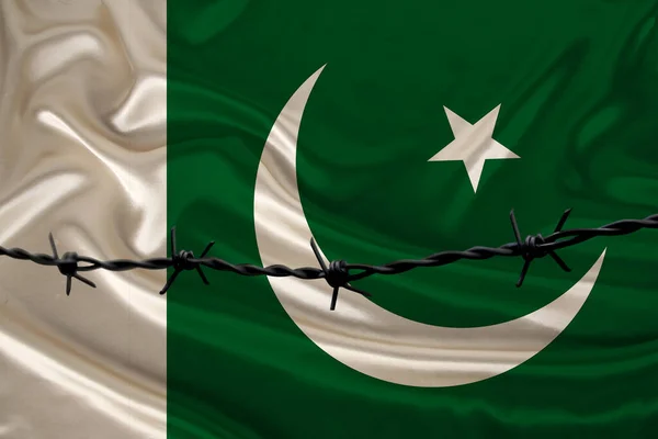 Fil de fer barbelé dans le contexte du drapeau national de soie de l'État du Pakistan, concept d'emprisonnement pour les délinquants, pour la zone de siège — Photo