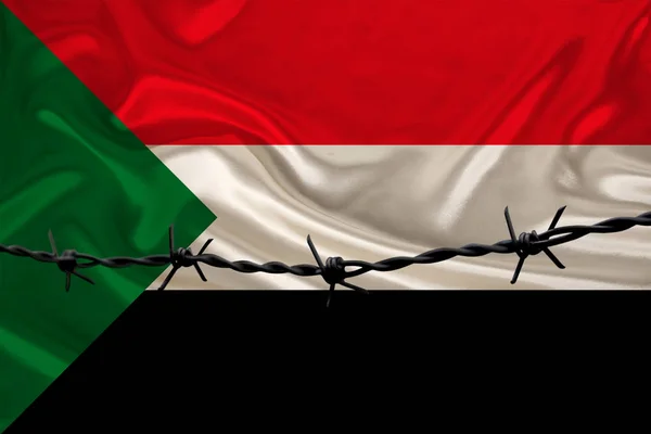 Arame farpado de ferro contra o pano de fundo da bandeira nacional da seda do Estado do Sudão, conceito de prisão para criminosos, para a área de cerco — Fotografia de Stock