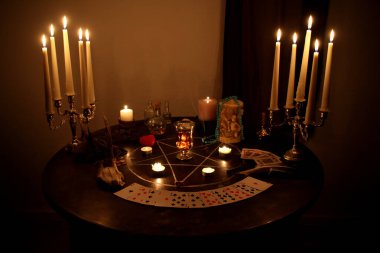 Mumlar yuvarlak bir masanın karanlık bir odasında, gümüş şamdanlarda, falcılık kartları seriliyor, bir pentagram çiziliyor, bir sihir ve büyücülük konsepti.