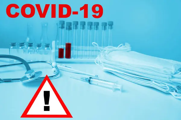 Медицинская лабораторная пробирка с кровью внутри, стетоскоп, шприц, защитные маски, концепция опасности распространения вируса коронавируса COVID-19 — стоковое фото