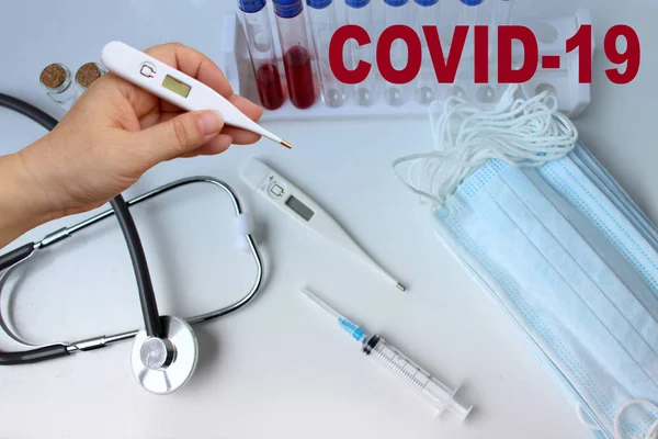 Медицинская лабораторная пробирка с кровью внутри, стетоскоп, шприц, защитные маски, концепция опасности распространения вируса коронавируса COVID-19 — стоковое фото