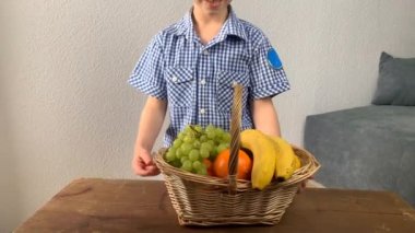 Çocuk elinde bir sepet meyve ve sebzeyle ahşap bir masada yuvarlanıyor. Dükkanda çocuk oyunu konsepti, alışveriş.