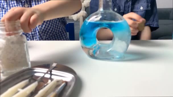 子供たち小学生の男の子がガラスのフラスコに色のついた液体を注ぎピペットと注射器から滴り落ちる幼児教育の概念 4Kスローモーション撮影 — ストック動画