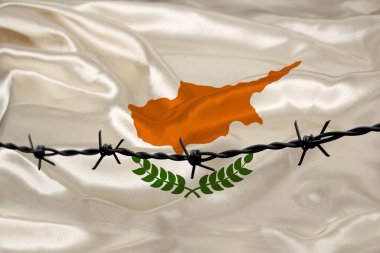 Kıbrıs devletinin ulusal ipek bayrağının arkasına dikenli demir teller geriliyor. Suçlular için, kuşatma bölgesi için hapis kavramı.