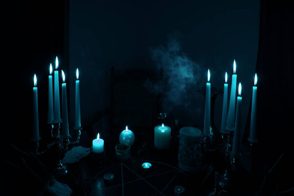 in a dark room on a round esoteric table candles burn, smoke, animal skulls lie, a pentagram is drawn, a red heart model, candles, a concept of magic, witchcraft