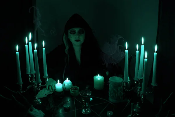 Female Fortuneteller conjures in a dark room, candles are burning on a round esoteric table with a pentagram, animal skulls lie, the concept of magic, witchcraft