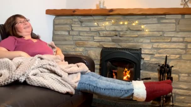 女性は燃える石で革のソファの上に座って熱を楽しんで踊る笑顔コンセプト居心地の良い家 — ストック動画