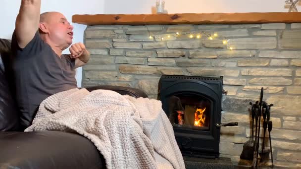 中年男子坐在一块燃烧的石头旁的皮革沙发上 享受着温暖 在感情上跳舞 一种好心情的概念 — 图库视频影像