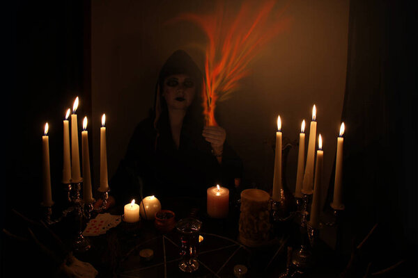 Female Fortuneteller conjures in a dark room, candles are burning on a round esoteric table with a pentagram, animal skulls lie, the concept of magic, witchcraft