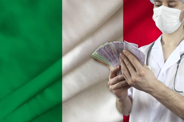 doctor with a stethoscope holds euro banknotes on the background of the silk national flag of Italy, the concept of medical insurance, budget, cost of treatment, organ donation