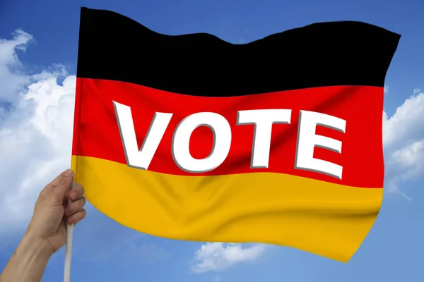 手は雲のある空の背景を背景に布の質感にドイツの色旗波のある絹投票という言葉で — ストック写真