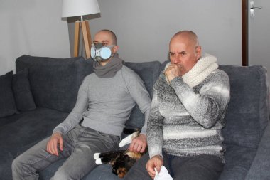 İki adam, hasta bir baba ve oğlu solunum cihazında bir odada kedili bir kanepede oturuyorlar. Virüs enfeksiyonu, grip...