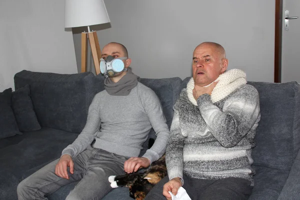 two men, a sick father and son in a respirator are sitting in a room on a sofa with a cat, the concept of a viral infection, flu