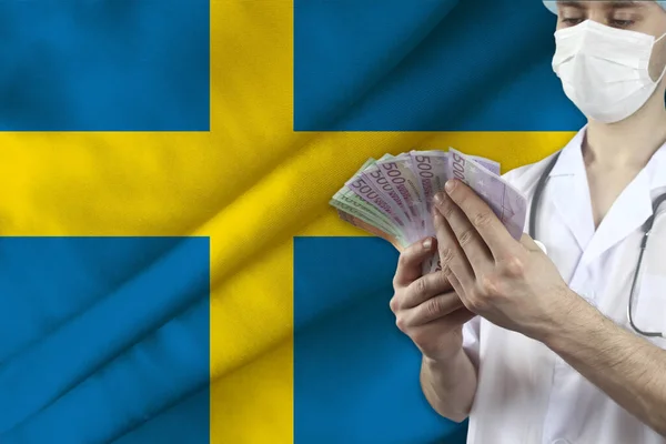 doctor with a stethoscope holds euro banknotes on the background of the silk national flag of Sweden, the concept of medical insurance, budget, cost of treatment, organ donation