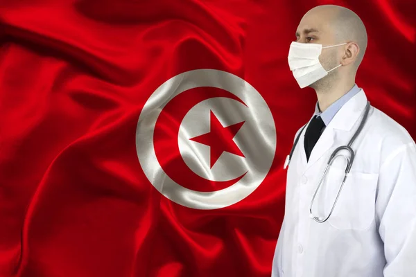 male doctor with a stethoscope on the background of the silk national flag of Tunisia, concept of national medical care, health, insurance, tourism