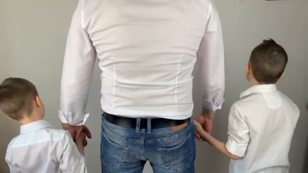 白いシャツを着た若い男は2人の息子の手を握っている良い家族の概念は彼の背中に立っている — ストック動画