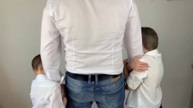 Beyaz gömlekli genç adam iki küçük oğluna sarılıyor, iyi bir aile kavramı, arkasını kolluyor.