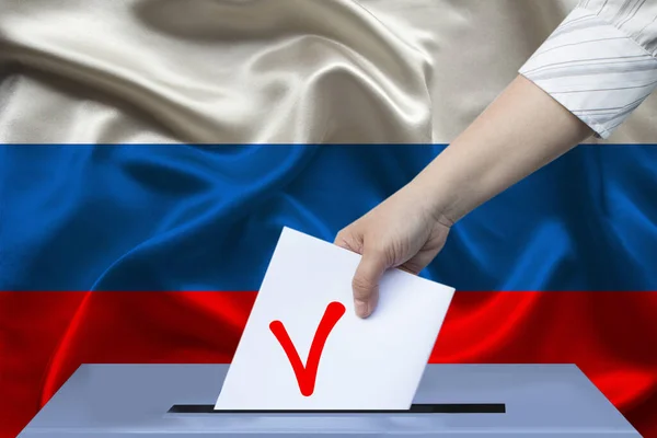 投票者の女性の手は ロシアの国旗 国家選挙の概念を背景に投票箱の投票を下げます — ストック写真