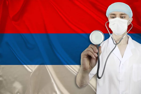 male doctor with a stethoscope on the background of the silk national flag of Serbia, the concept of national medical care, health, insurance, tourism