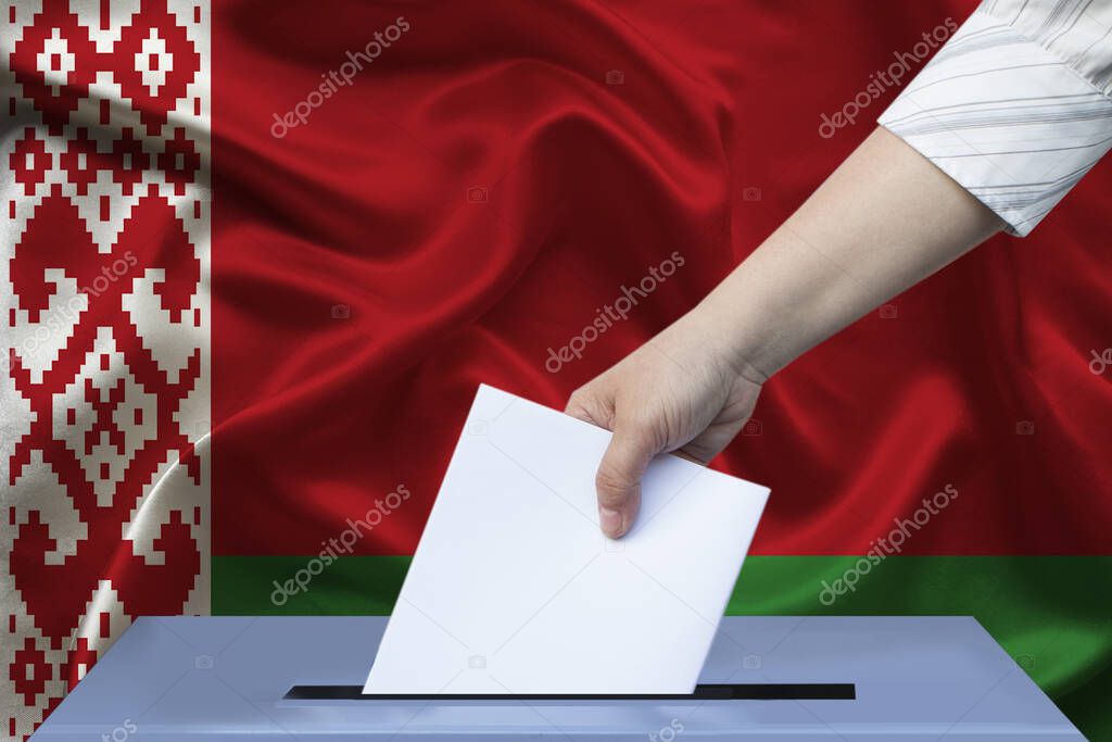 Voters female hand lowers the ballot in the ballot box against the background of the national flag of Belarus, concept of state elections     